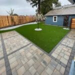 Backyard of Blue house with Checkered walkway and golf-ready grass.