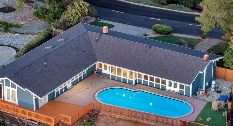 Drone view of L-shaped house with shingles and a pool